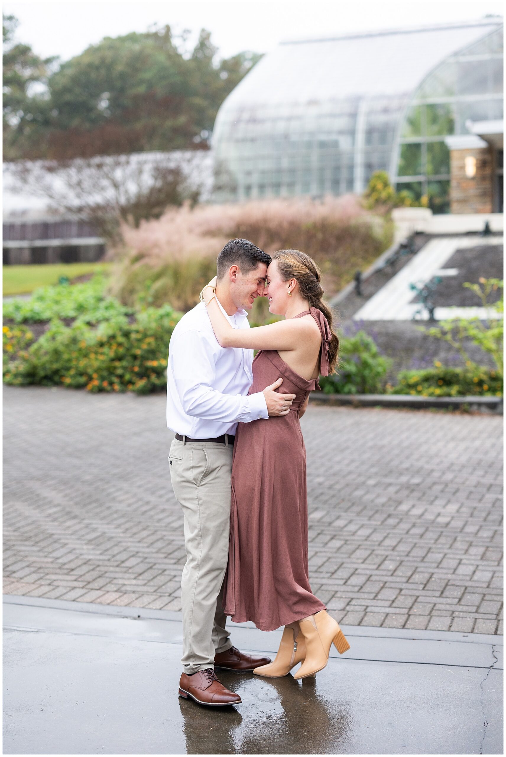 Catherine and Jake hold each other and smile in front of the Botanical Garden's greenhouse. 