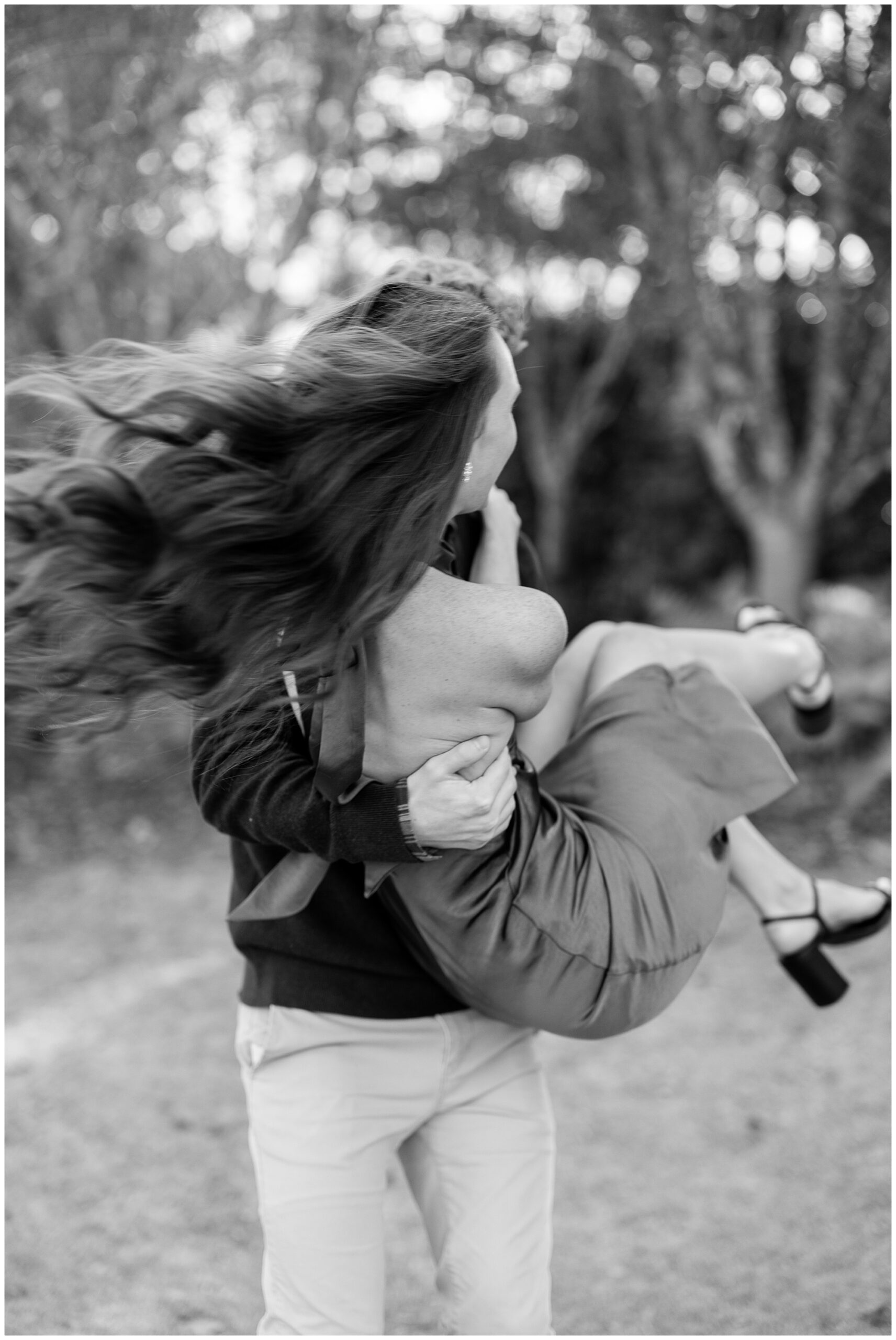 A black and white image of Camden picking Olivia up and swinging her around in the air. 