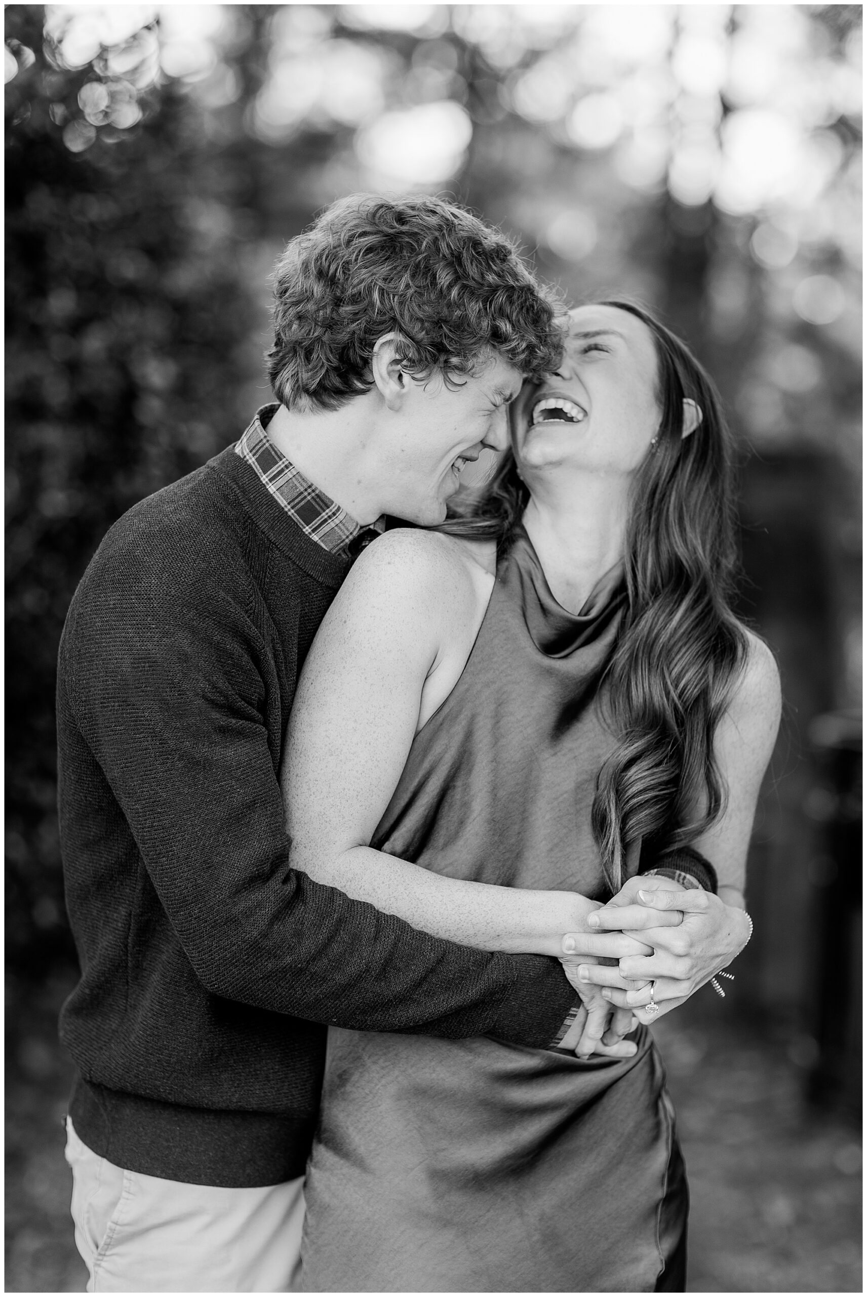 A black and white image of Camden holding Olivia from behind while they laugh with each other. 