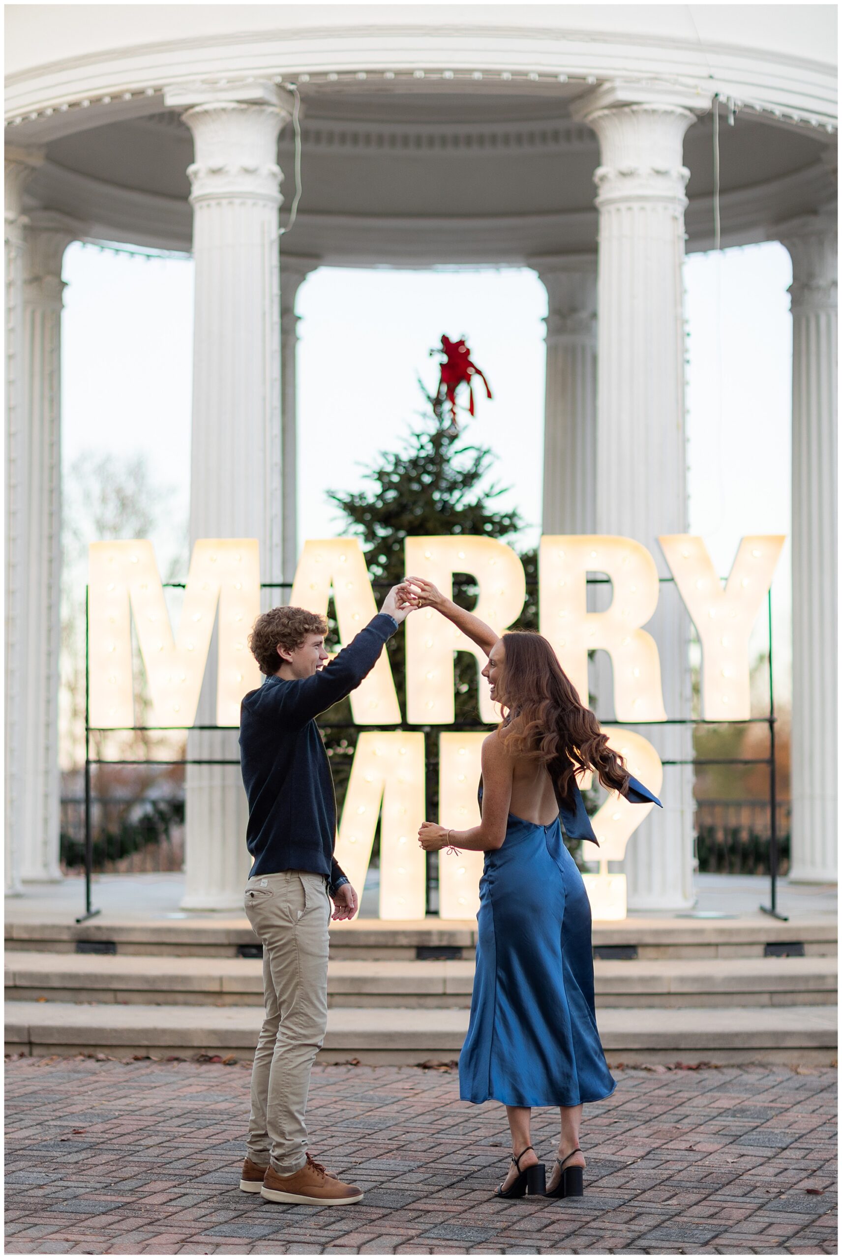 Camden spins Olivia around as they dance in front of the "Marry Me?" sign. 